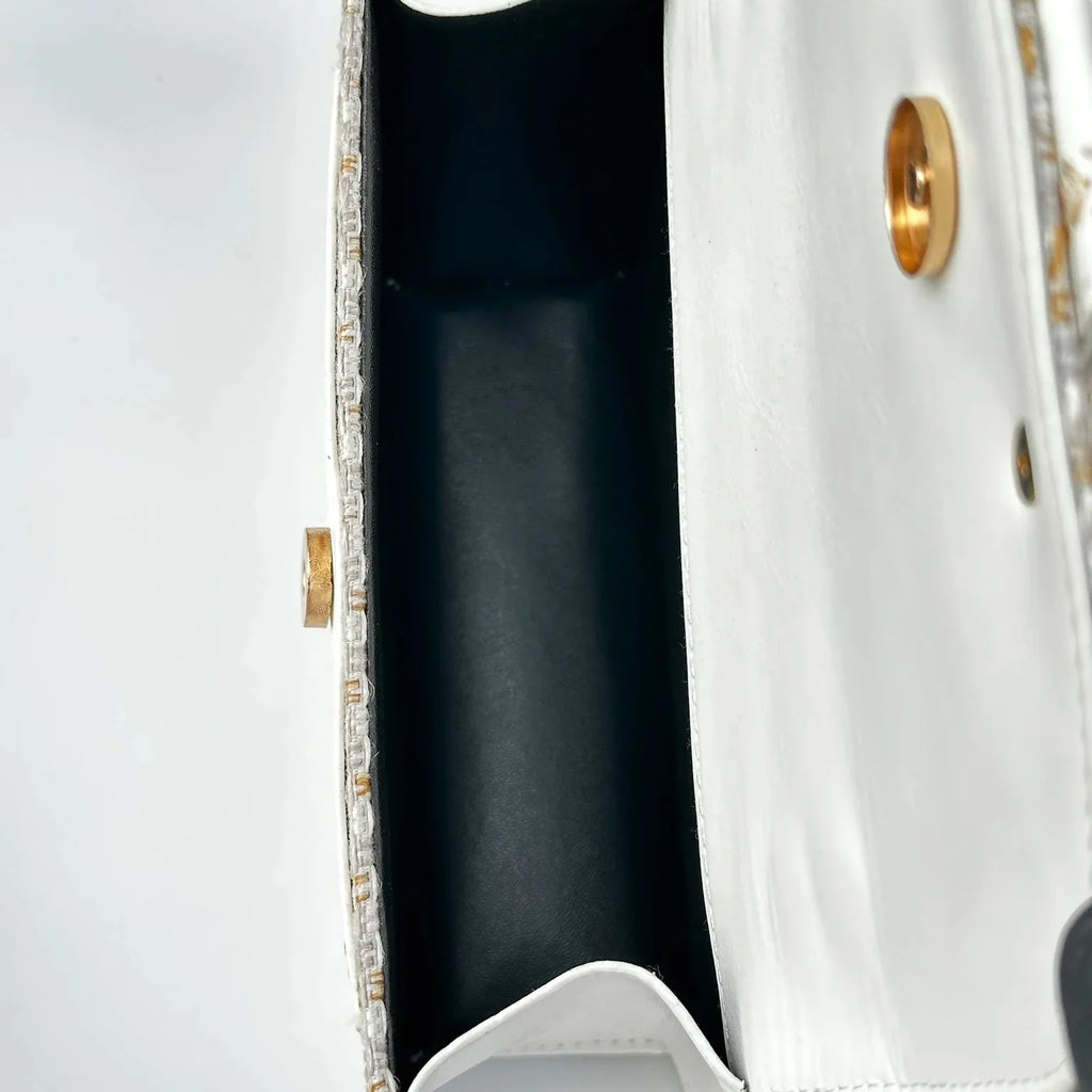 Close-up of a white handbag with gold accents on a light gray background