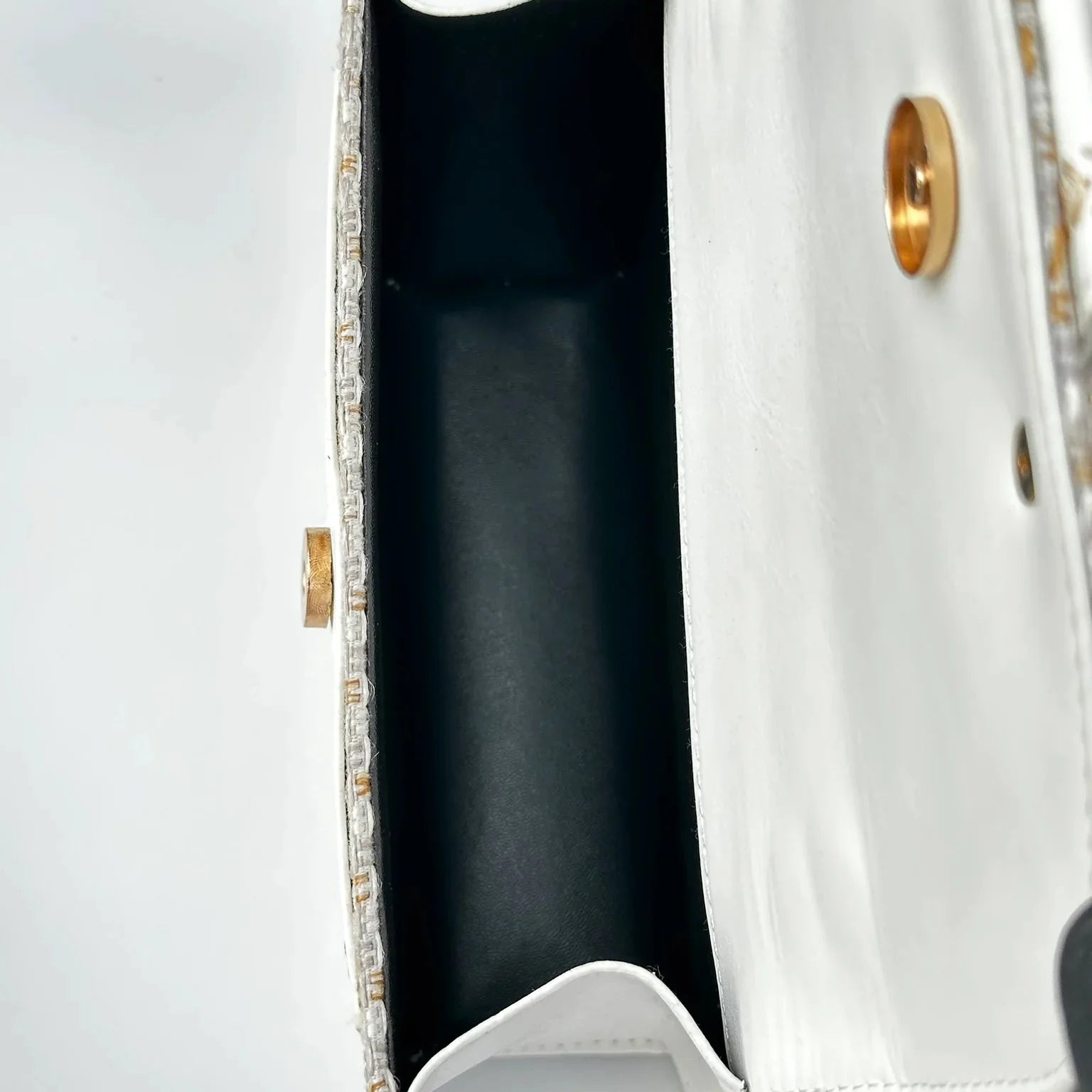 Close-up of a white handbag with gold accents on a light gray background