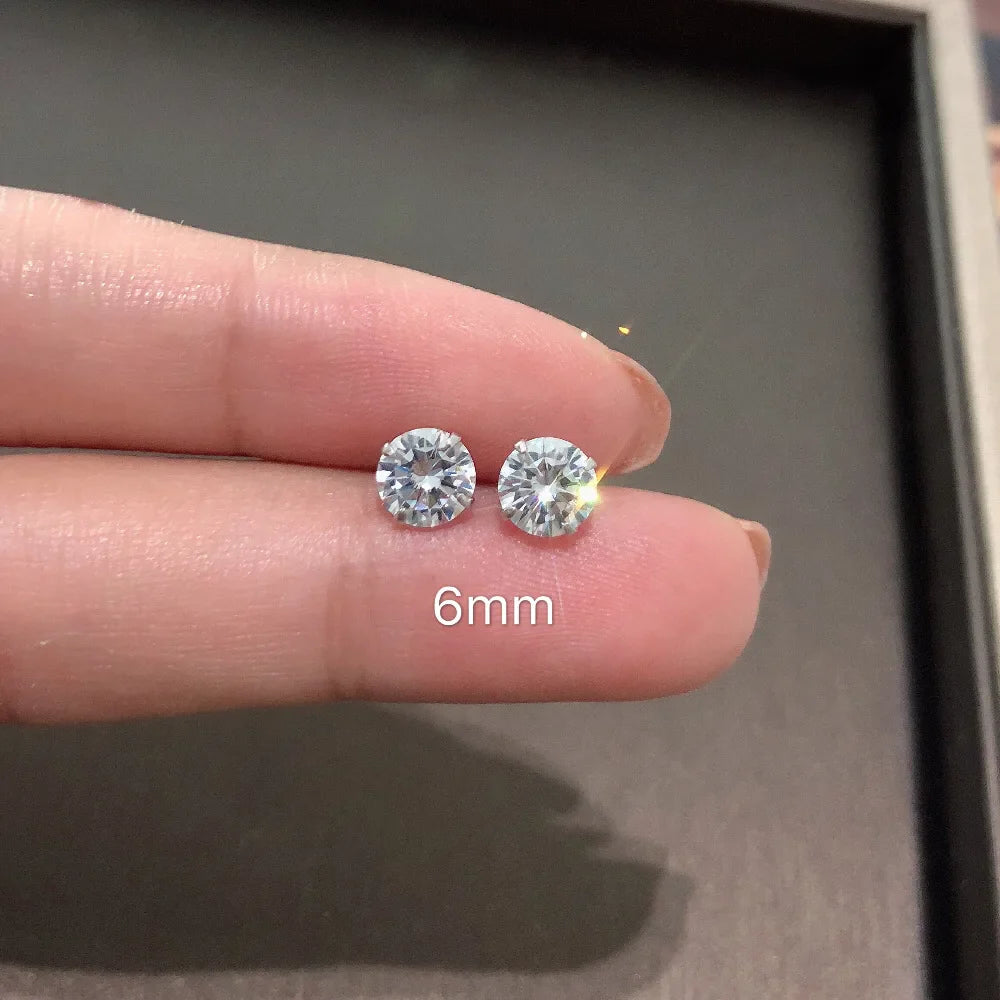 Diamond stud earrings held between fingers with a measurement label '6mm' on a neutral background
