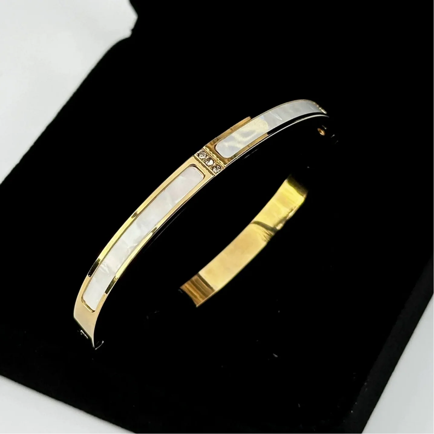 Gold and silver bangle on a black stand with a white background