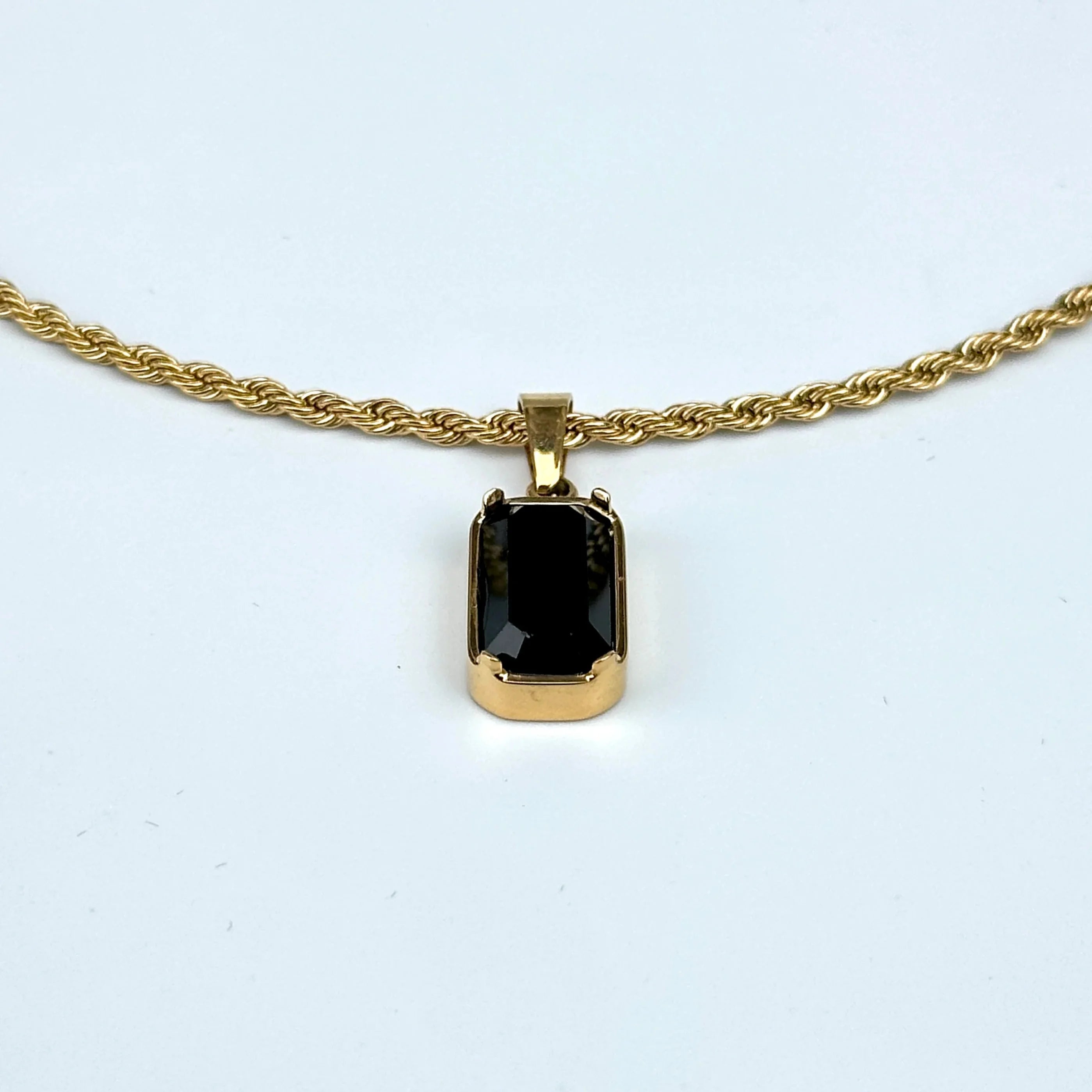 Gold necklace with a black pendant on a white background