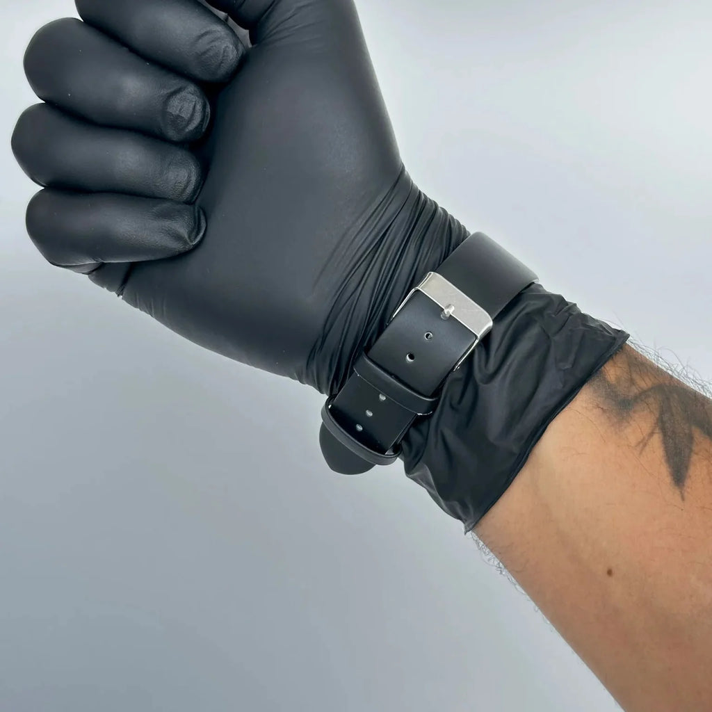 Hand wearing a black glove with a silver watch on a gray background
