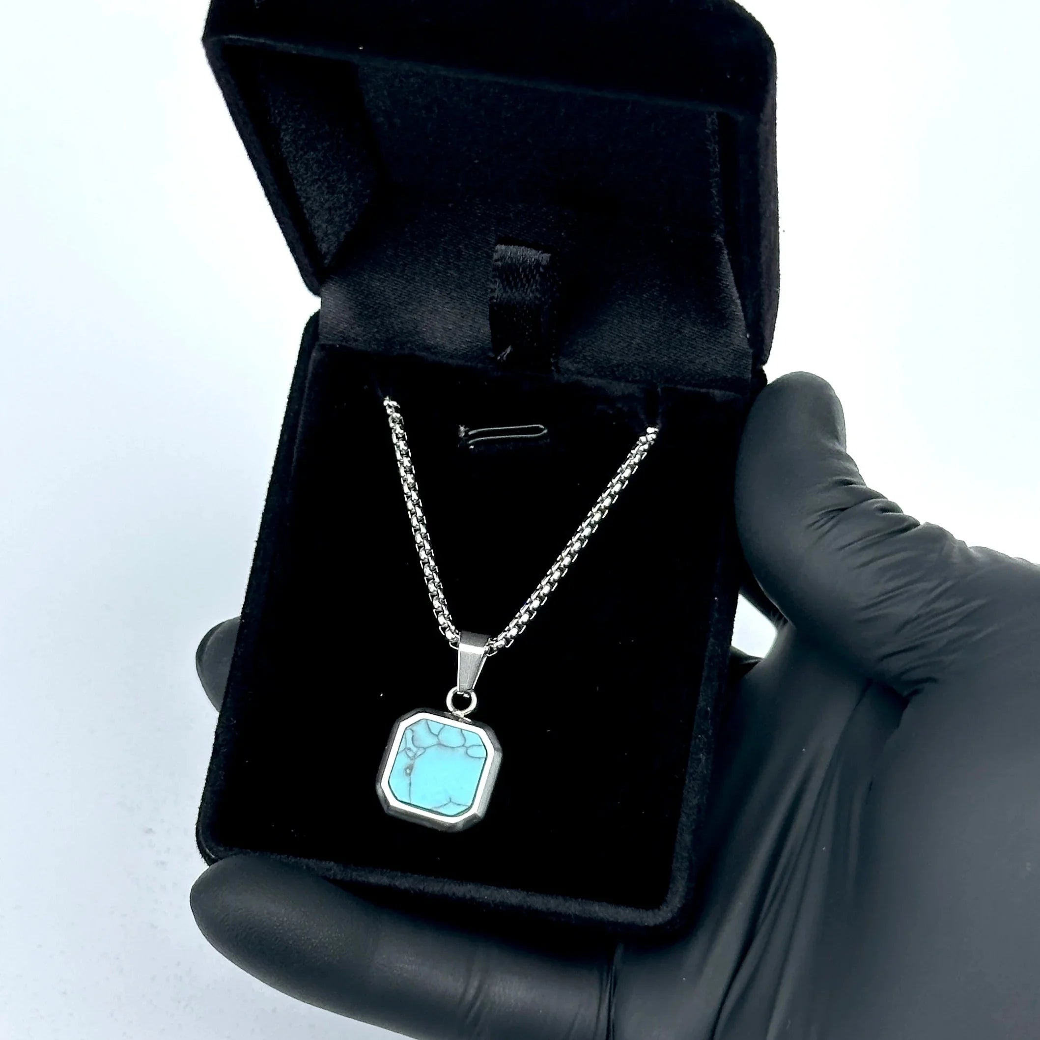 Necklace with a blue pendant held by a gloved hand on a white background