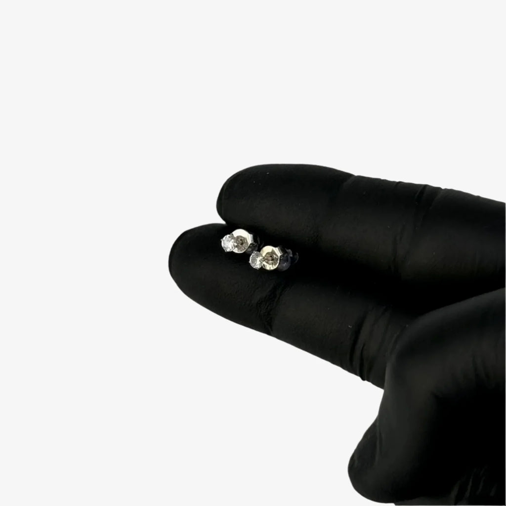 Pair of silver earrings held between two fingers wearing black gloves on a gray background