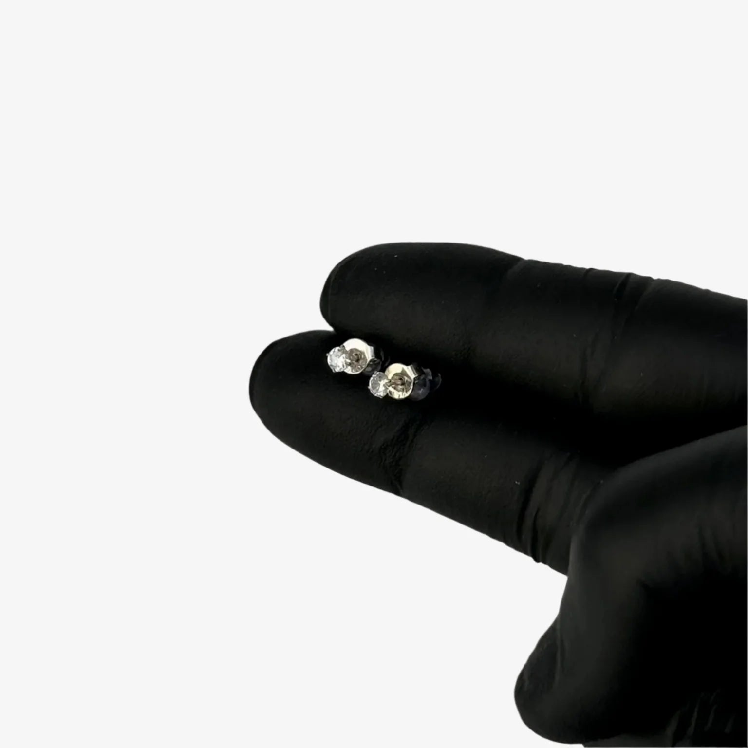 Pair of silver earrings held between two fingers wearing black gloves on a gray background