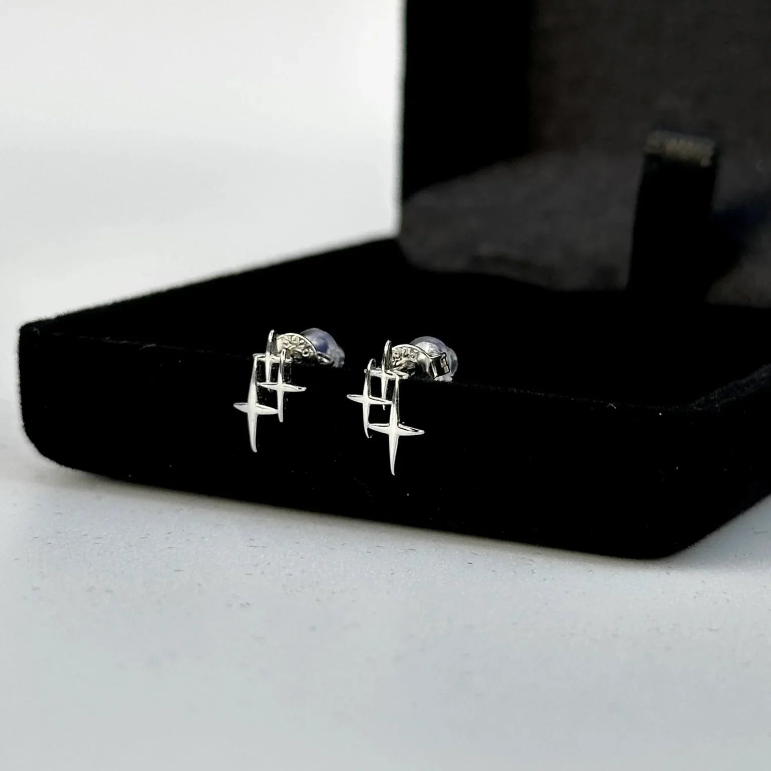Pair of silver earrings on a black jewelry box against a white background