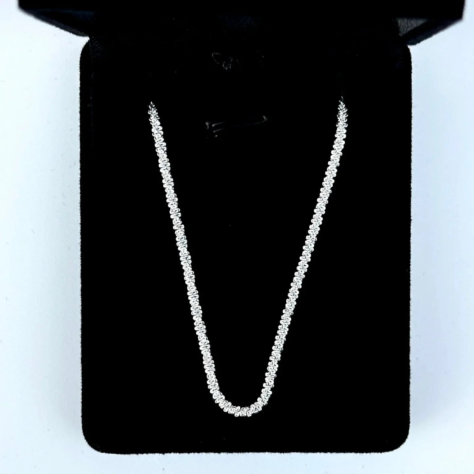 Silver chain necklace on a black stand with a white background