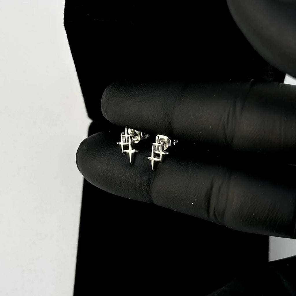 Silver earrings held in black gloves against a white background