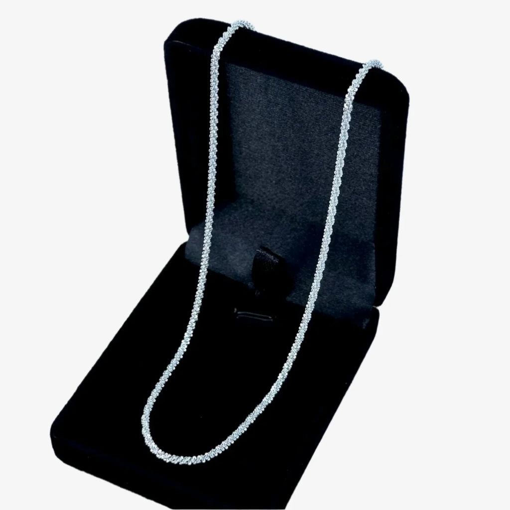 Silver necklace on a black velvet stand against a light blue background