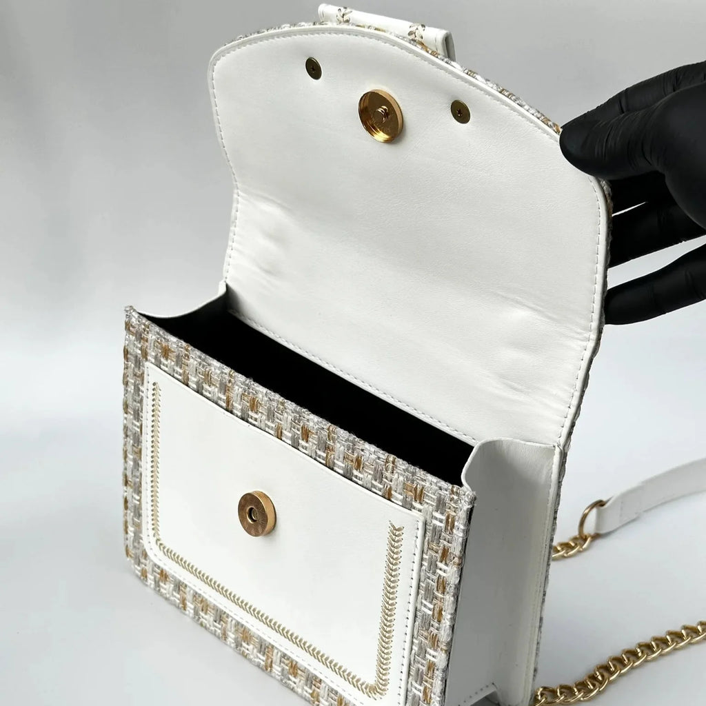 White handbag with decorative gold accents on a light gray background