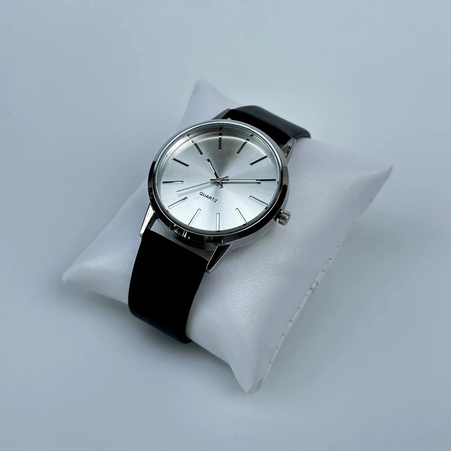 Wristwatch with black strap on a white cushion against a light gray background